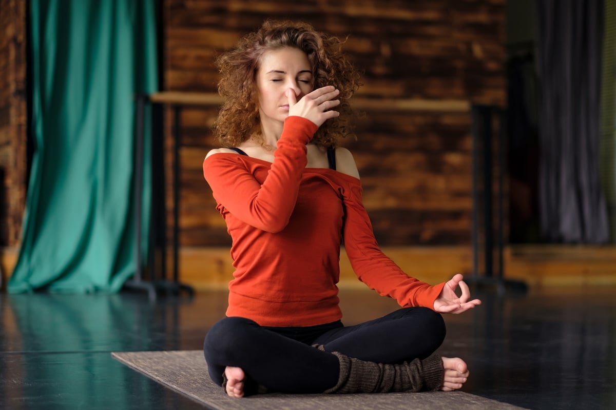 Young curly woman doing yoga exercises, using nadi shodhana pranayama